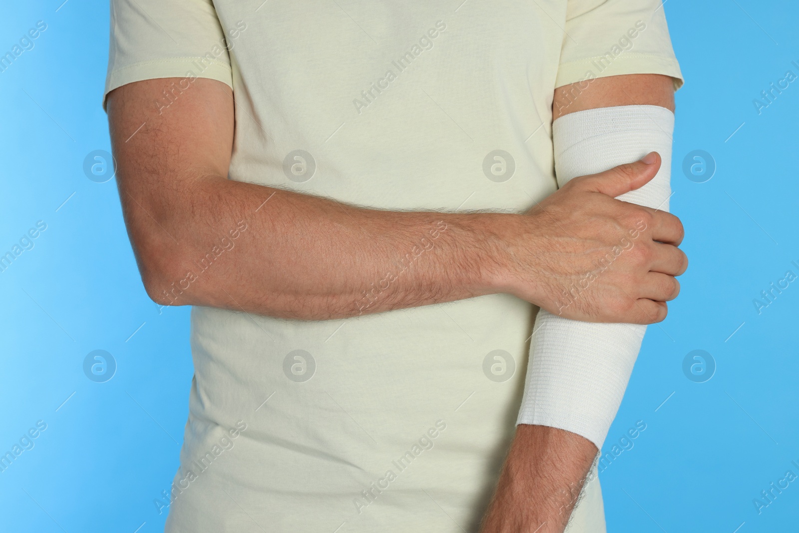 Photo of Man with arm wrapped in medical bandage on light blue background, closeup