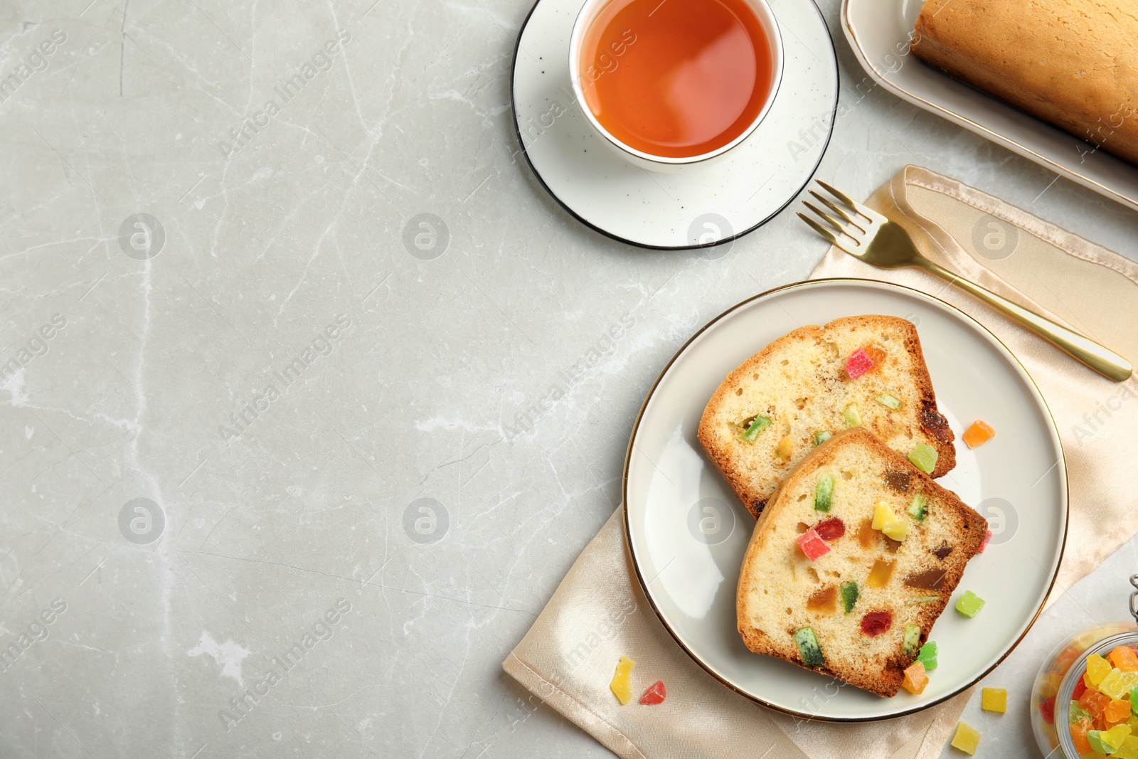 Photo of Delicious cake with candied fruits and tea on light table, flat lay. Space for text