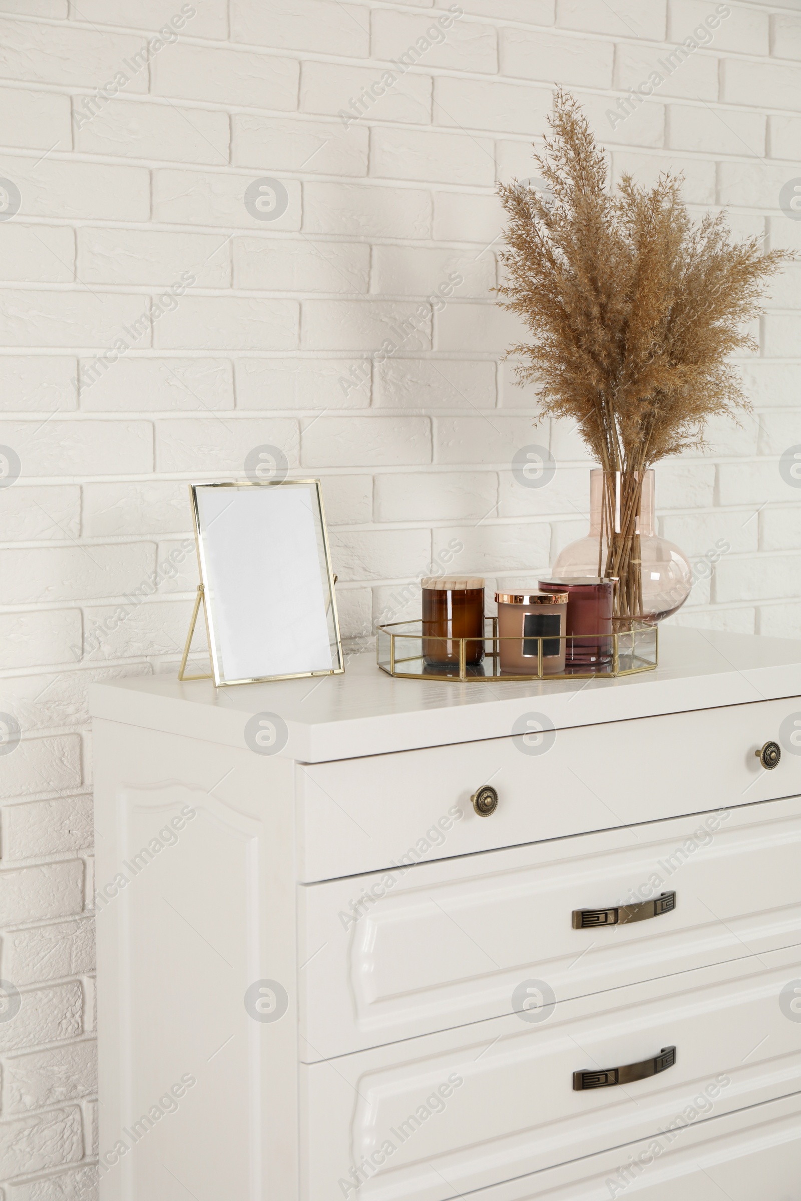 Photo of Modern chest of drawers with decor near white brick wall