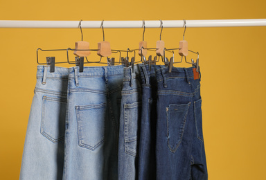 Photo of Rack with different jeans on yellow background