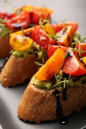 Photo of Delicious bruschettas with avocado, tomatoes and balsamic vinegar on gray plate, closeup