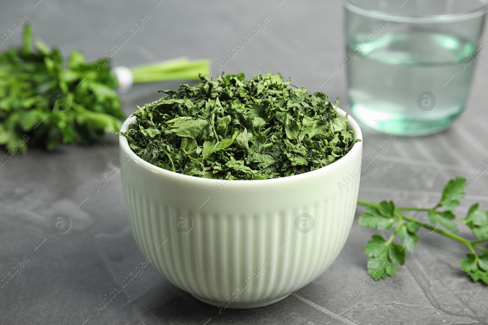 Photo of Bowl with dried parsley on grey stone table, closeup