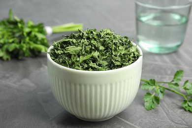 Bowl with dried parsley on grey stone table, closeup