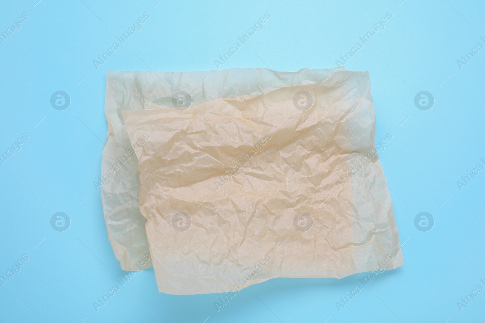 Photo of Sheets of crumpled baking paper on light blue background, top view