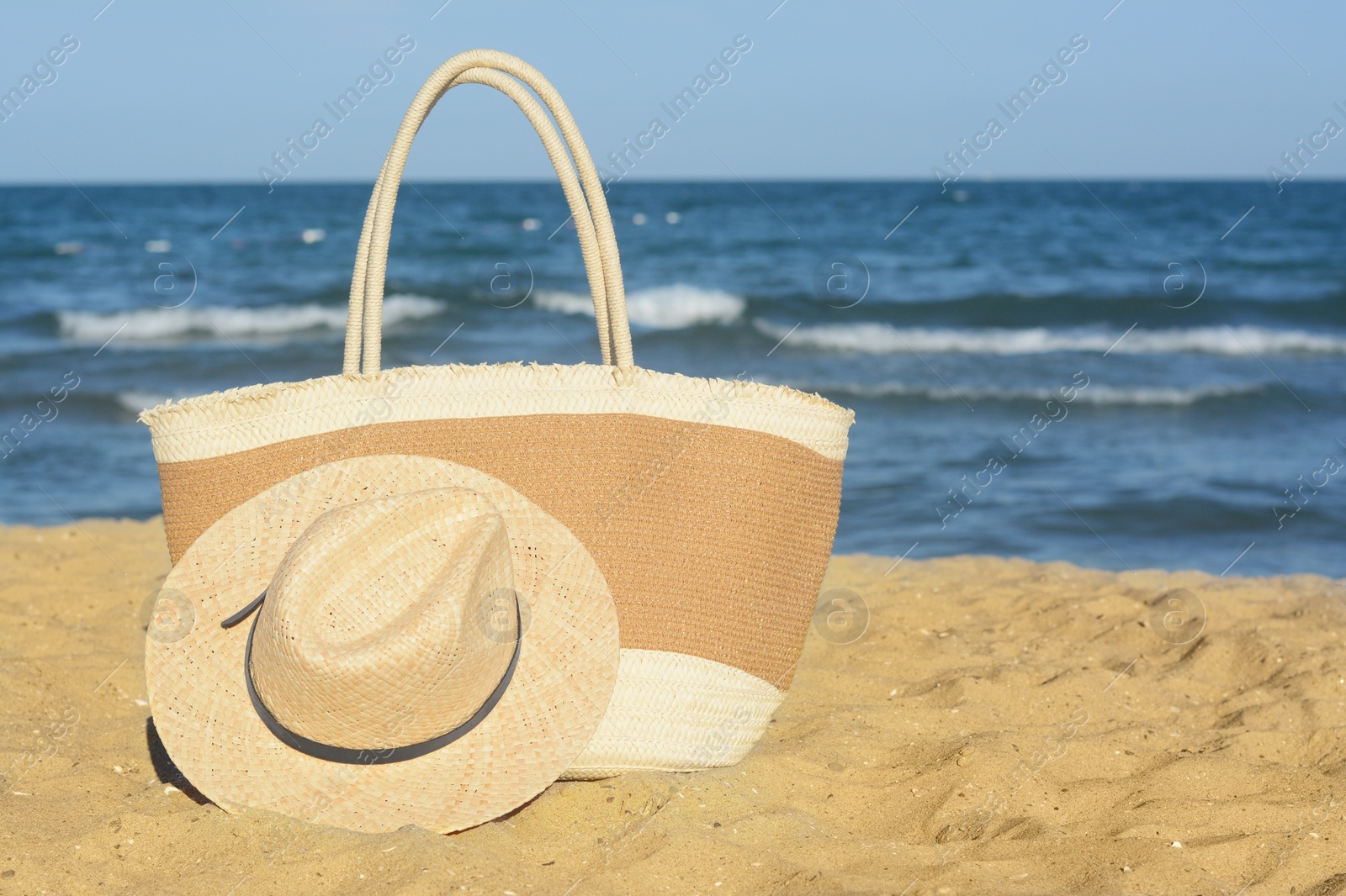 Photo of Stylish bag and hat near sea on sunny day, space for text. Beach accessories