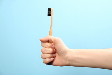Photo of Woman holding bamboo toothbrush on light blue background, closeup