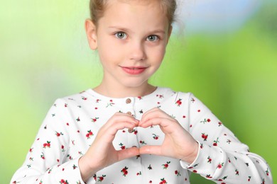 Cute little girl making heart with hands on blurred background, closeup