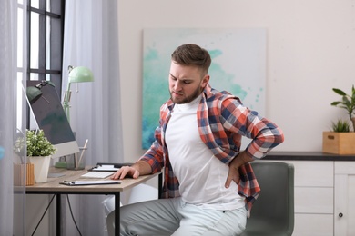 Photo of Young man suffering from back pain in office