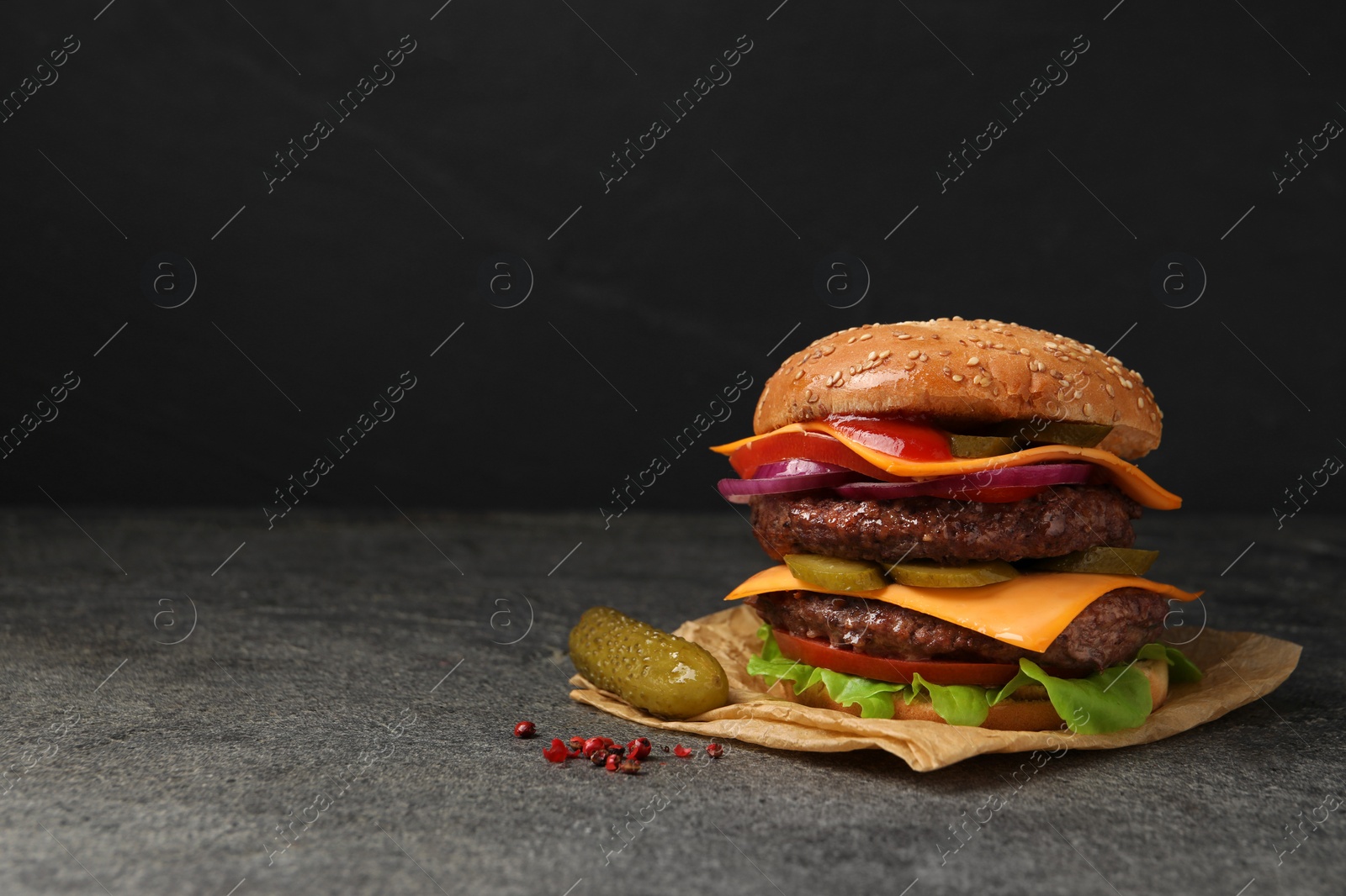 Photo of Delicious burger with meat cutlets, cheese, pickled cucumbers and lettuce on grey table, space for text