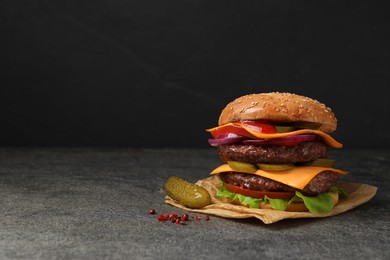 Delicious burger with meat cutlets, cheese, pickled cucumbers and lettuce on grey table, space for text