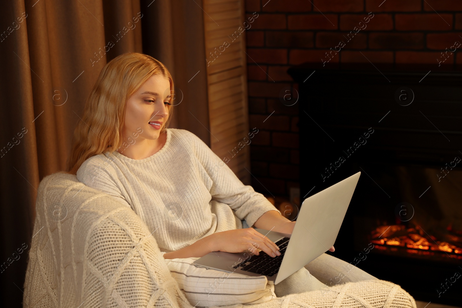 Photo of Young woman working on laptop near fireplace in room