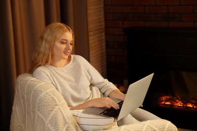 Young woman working on laptop near fireplace in room