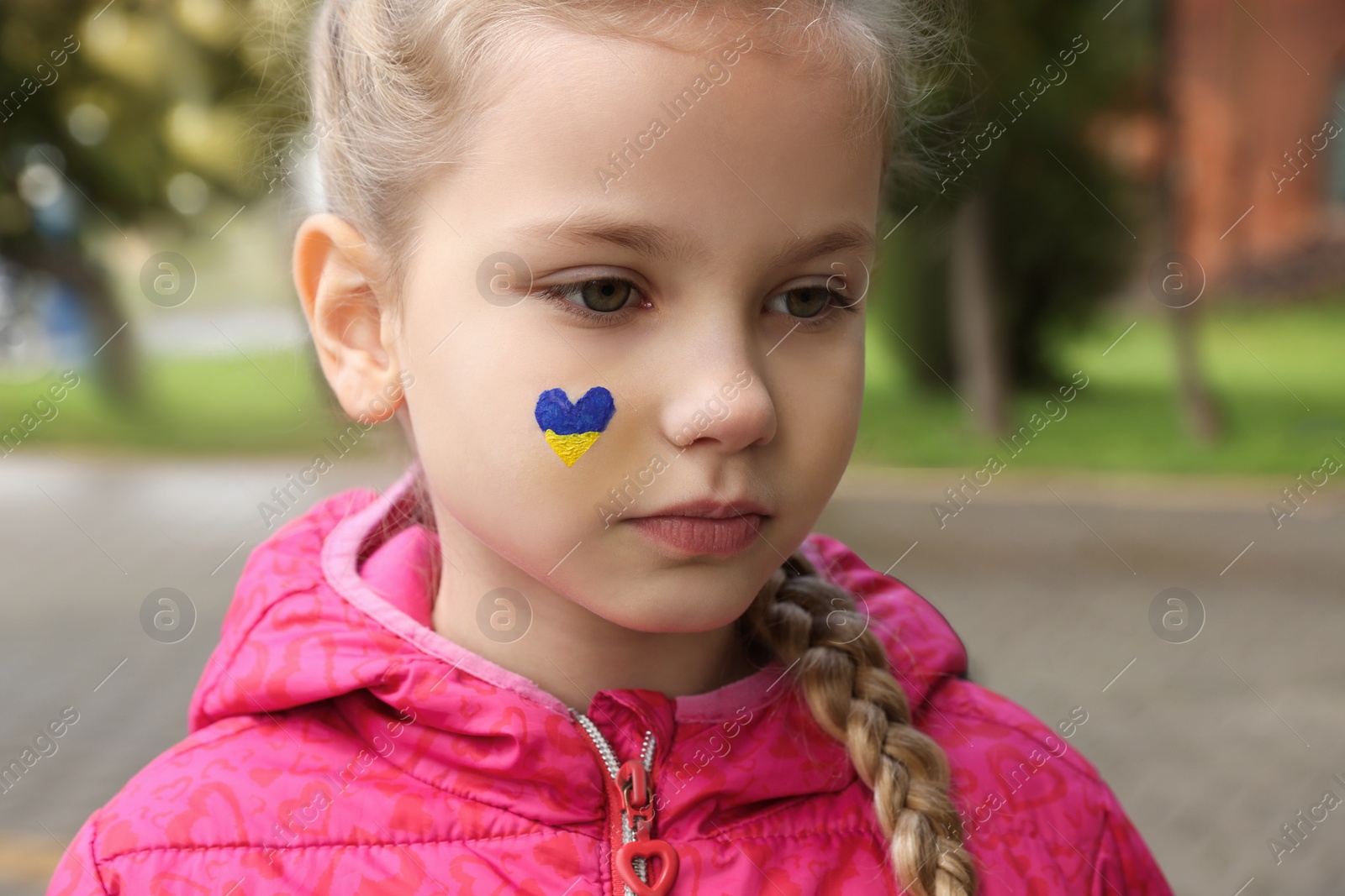 Photo of Little girl with drawing of Ukrainian flag on face in heart shape outdoors