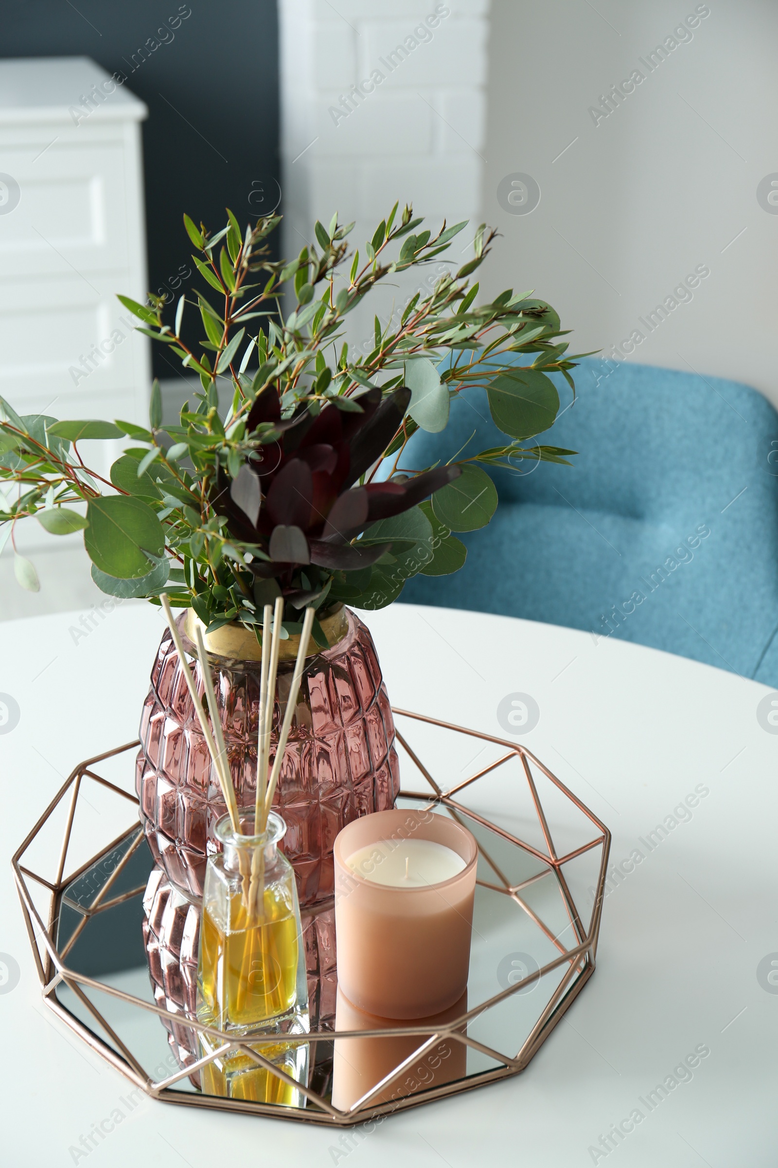 Photo of Beautiful bouquet with eucalyptus branches, candle and aromatic reed air freshener on white table indoors. Interior elements