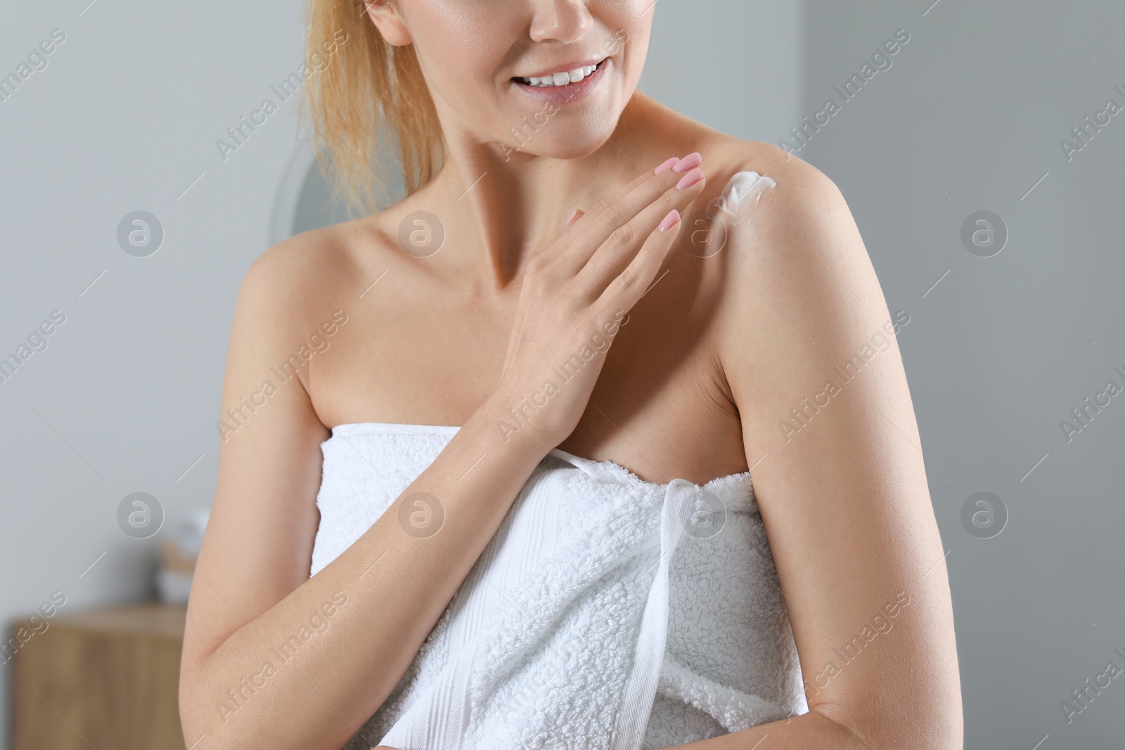 Photo of Woman applying body cream onto shoulder indoors, closeup