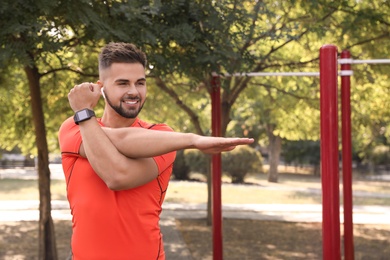 Young man with wireless headphones listening to music while exercising on sports ground. Space for text