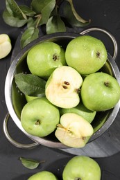 Photo of Ripe green apples with water drops and leaves on black table, top view
