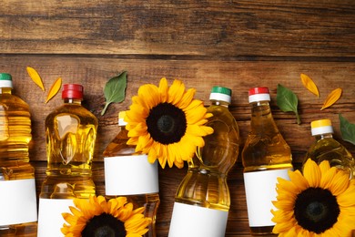 Bottles of sunflower cooking oil and beautiful flowers on wooden table, flat lay. Space for text