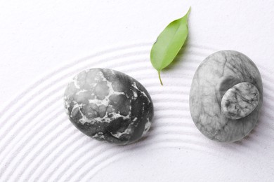 Photo of Zen garden stones and leaf on white sand with pattern, flat lay