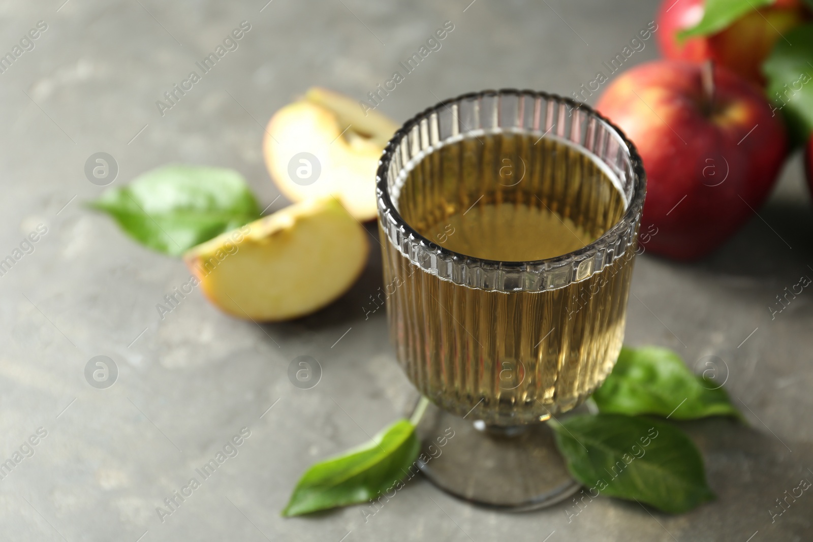 Photo of Glass of delicious cider, green leaves and apples on gray table, closeup. Space for text