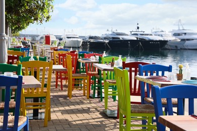 Beautiful view of outdoor cafe with colorful wooden chairs near pier