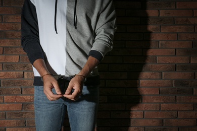 Photo of Male criminal in handcuffs near brick wall, closeup. Space for text
