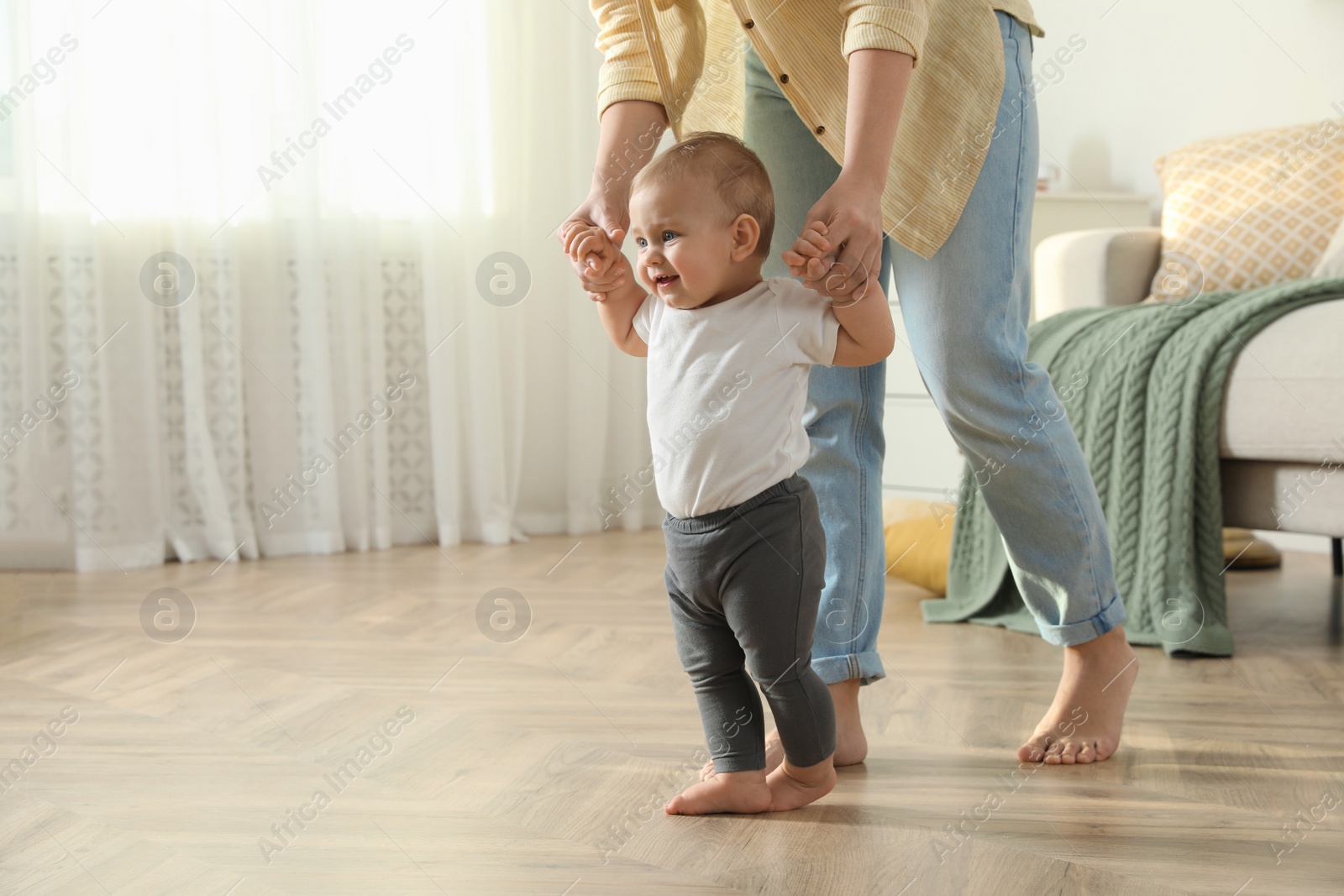 Photo of Mother supporting her baby daughter while she learning to walk at home