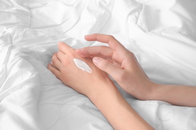 Young woman applying cream onto hands, indoors