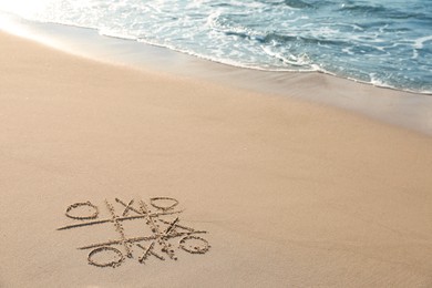 Tic tac toe game drawn on sand near sea, space for text