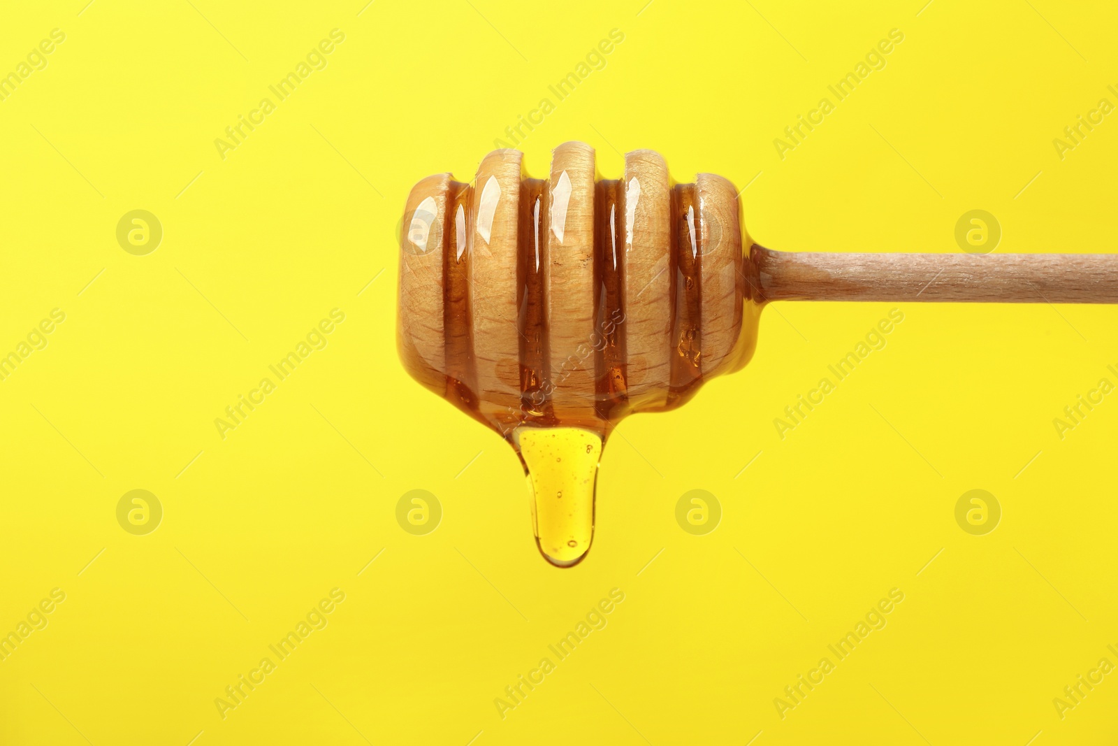 Photo of Delicious honey flowing down from dipper against yellow background, closeup