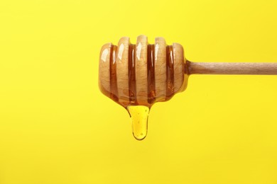 Delicious honey flowing down from dipper against yellow background, closeup