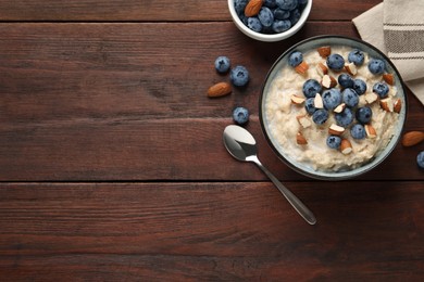 Photo of Tasty oatmeal porridge with blueberries and almond nuts served on wooden table, flat lay. Space for text