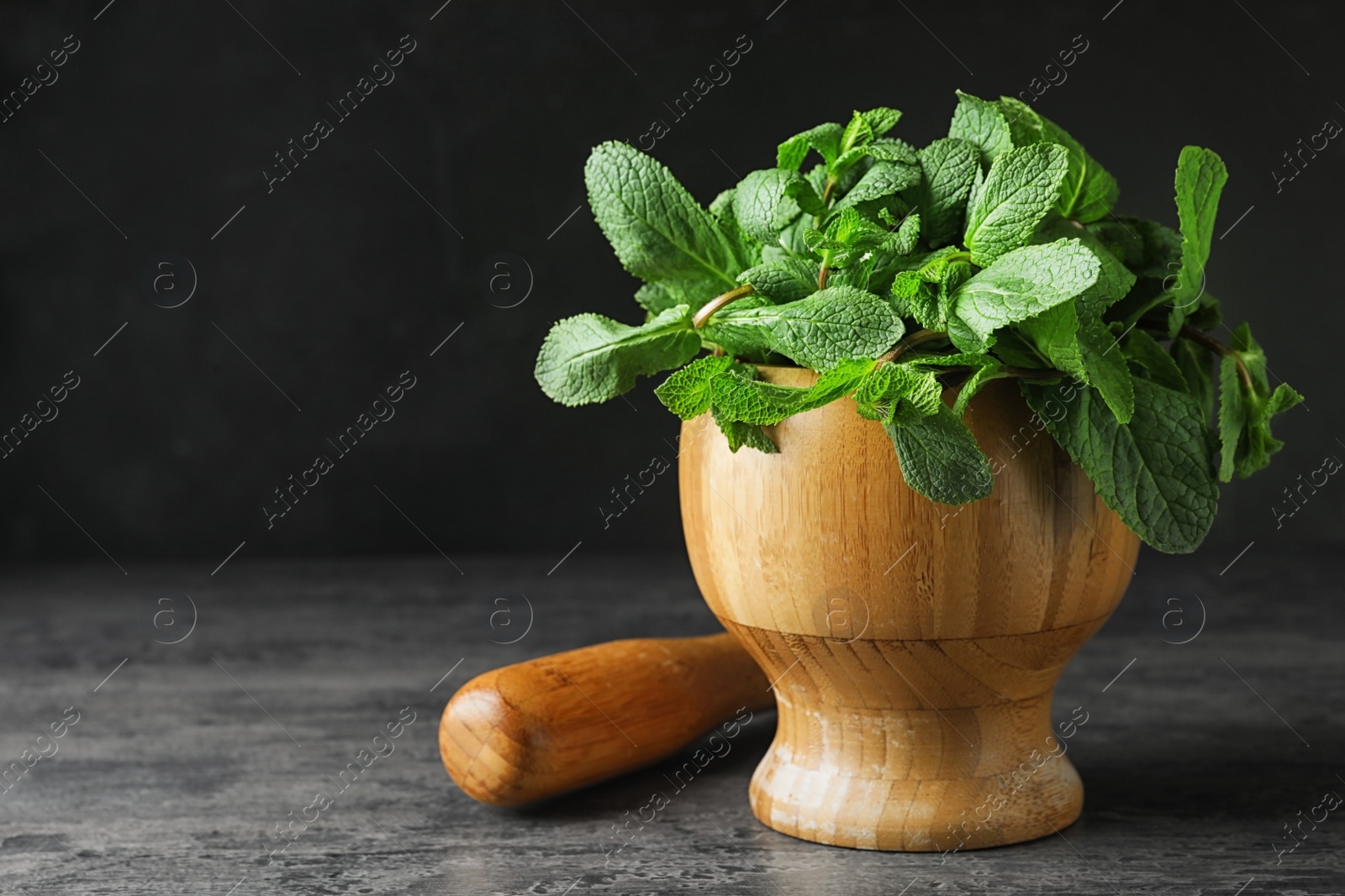 Photo of Wooden mortar full of fresh green mint on grey table against dark background