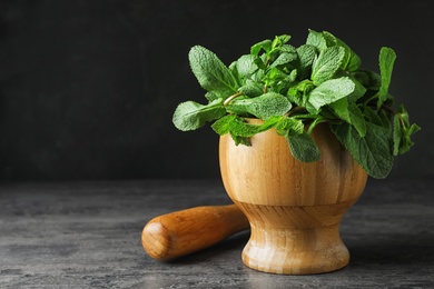 Photo of Wooden mortar full of fresh green mint on grey table against dark background