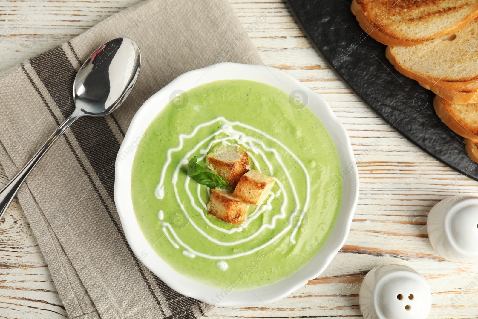 Photo of Delicious broccoli cream soup with croutons served on white wooden table, flat lay