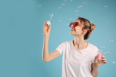 Photo of Young woman blowing soap bubbles on light blue background, space for text