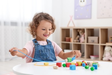 Photo of Motor skills development. Little girl playing with wooden pieces and string for threading activity at table indoors