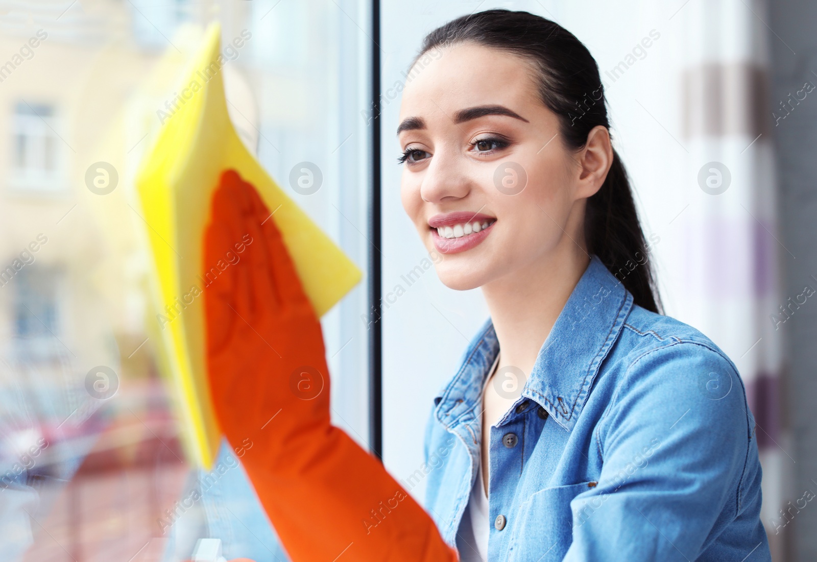 Photo of Young woman cleaning window glass at home