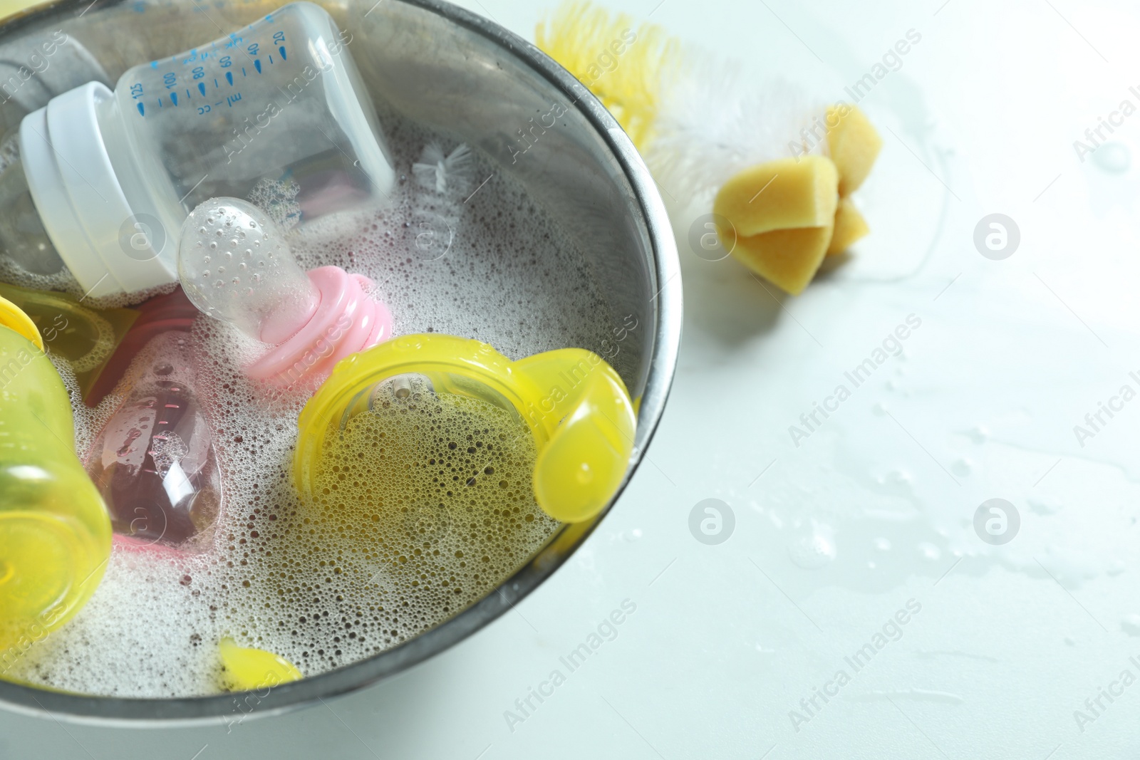 Photo of Metal bowl with baby bottles on white table, above view. Space for text