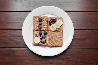 Different tasty toasts with nut butter and products on wooden table, top view