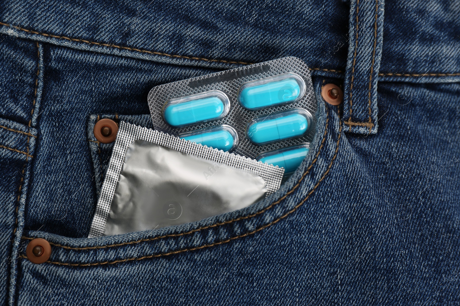 Photo of Jeans with pills and condom in pocket as background, top view. Potency problem concept