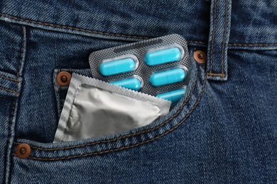 Jeans with pills and condom in pocket as background, top view. Potency problem concept