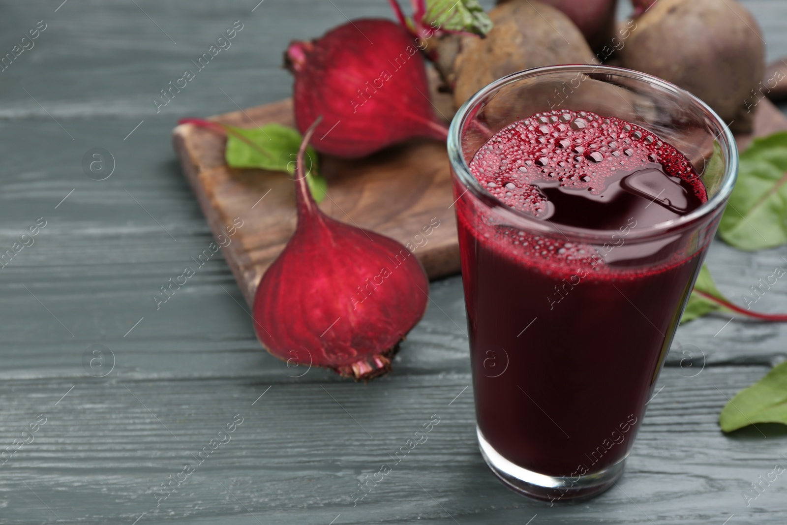 Photo of Fresh beet juice and raw vegetable on grey wooden table. Space for text