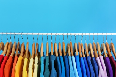 Rack with bright clothes on blue background, space for text. Rainbow colors