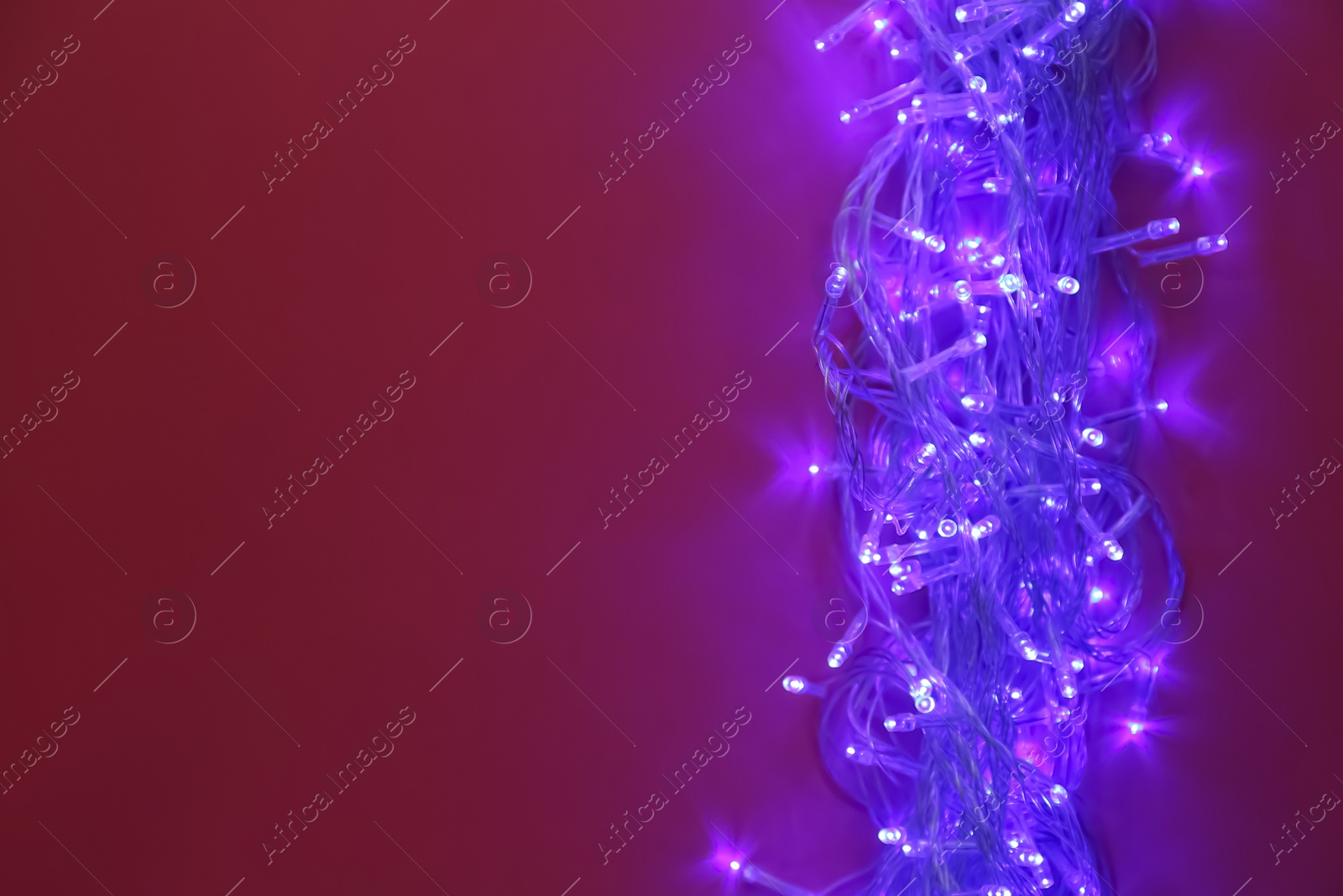 Photo of Glowing Christmas lights on burgundy background, top view. Space for text