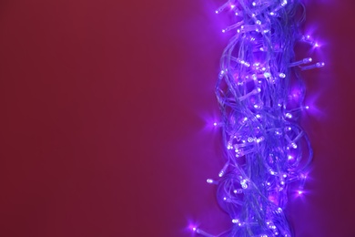 Photo of Glowing Christmas lights on burgundy background, top view. Space for text