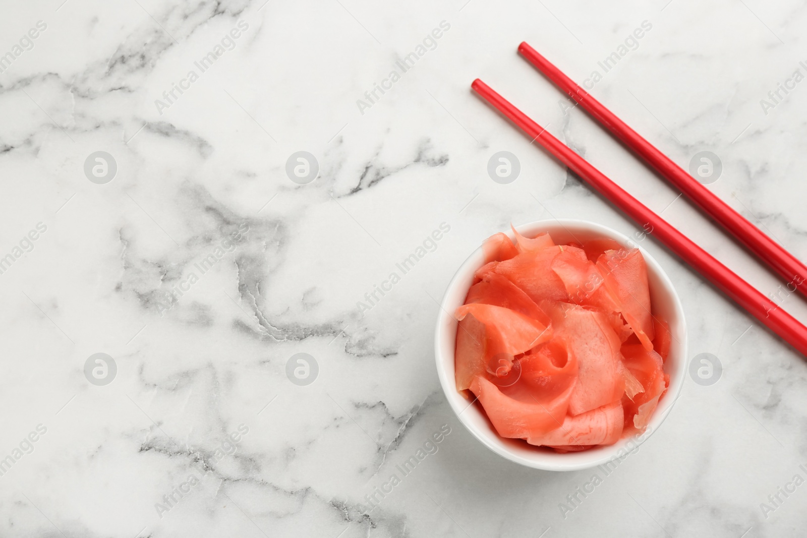 Photo of Spicy pickled ginger and chopsticks on white marble table, flat lay. Space for text