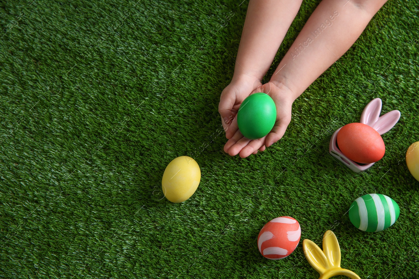 Photo of Little child holding painted Easter egg on green grass, top view. Space for text