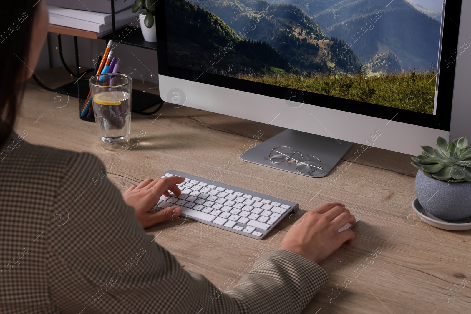 Photo of Woman working on computer at wooden table in room, closeup