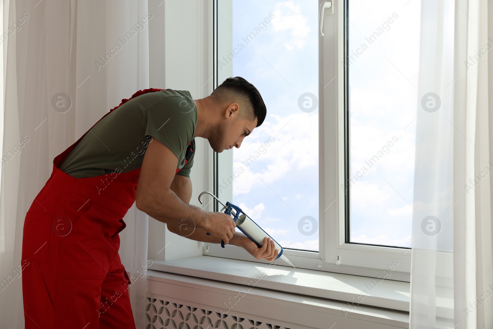 Photo of Construction worker sealing window with caulk indoors